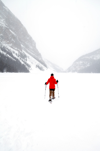 A woman snowshoes away from camera on a frozen lake, on a snowy day.