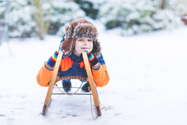 маленький мальчик, имеющих fung с санями ездить в зимний период - little boys sled clothing slide стоко�вые фото и изображения