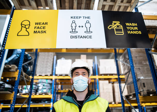 istock Young worker with face mask standing indoors in warehouse, coronavirus concept. 1282332988