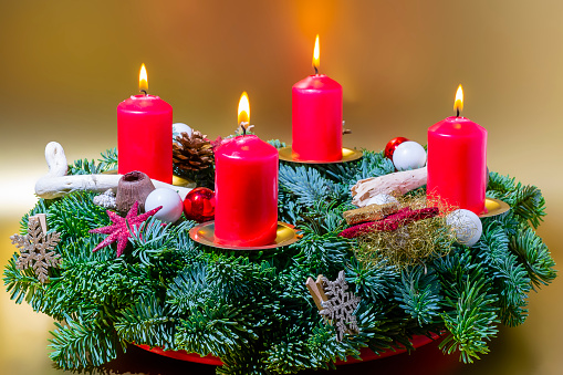 a decorated Christmas wreath with four burning red candles on the golden background. A Christmas wreath decorated with candles, stars, balls, strings. Christmas card.