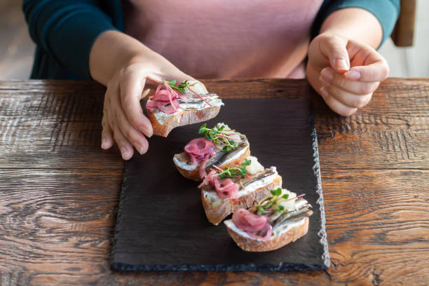 frau isst offene sandwiches mit geräuchertem fisch, frischkäse, kaviar und mikrogrün - bread cheese bruschetta canape stock-fotos und bilder