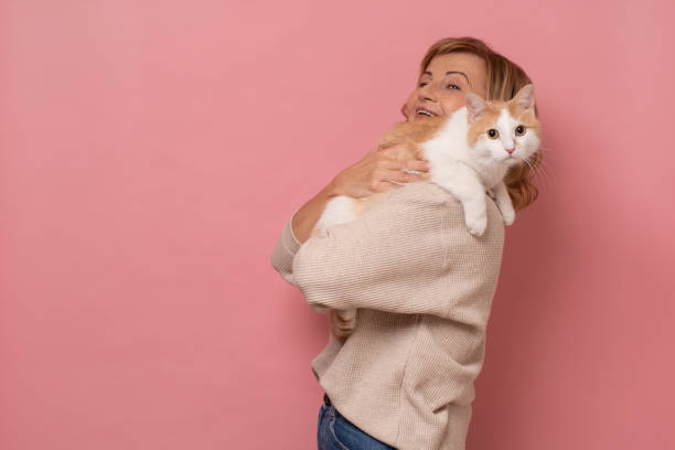 istock Mature woman lovingly hugging cat on pink wall. 1282338336