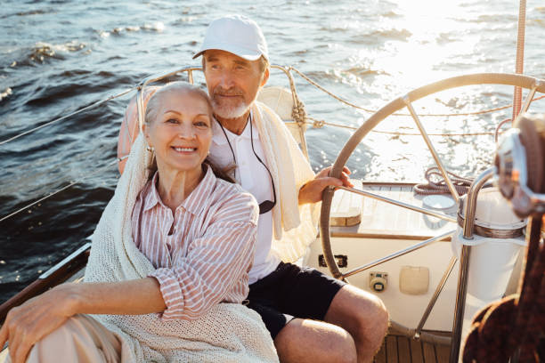 istock Smiling mature woman looking at camera while her husband steering a sailboat. Two senior people enjoying a vacation on yacht. 1282338527