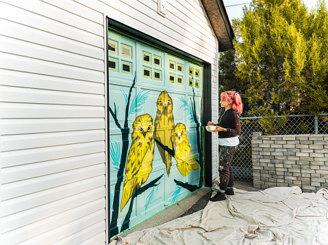 Female mural artist creating art on the garage door of the private home in the city.