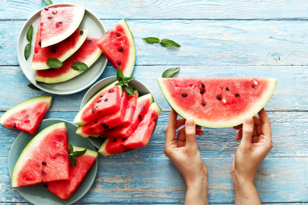 istock Fresh red watermelon slice in female hands on an blue rustic wood background with copy space. Watermelon slice and mint on the background. Top view 1282340370