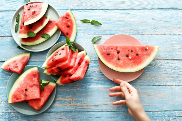 istock Fresh red watermelon slice in female hands on an blue rustic wood background with copy space. Watermelon slice and mint on the background. Top view 1282340373