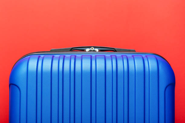 istock Modern blue suitcase on red background close up with copy space for text. Minimal style travel concept. Vacation trip. Summer holiday stock photo. Trendy color 2020 classic blue 1282340734
