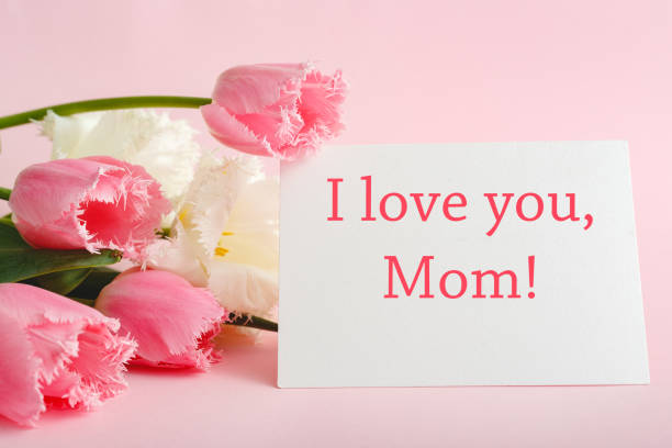 I love you Mom text on gift card in flower bouquet on pink background. Greeting card for Mom. Happy Mothers Day. Flower delivery.Congratulations card in flowers for women.Greeting card in pink tulips te amo texto de mamá en tarjeta de regalo en ramo de flores sobre fondo rosa. tarjeta de felicitación para mamá. feliz día de la madre. entrega de flores. tarjeta de felicitación en flores para mujeres. tarjeta de felicitación en tulipanes rosados