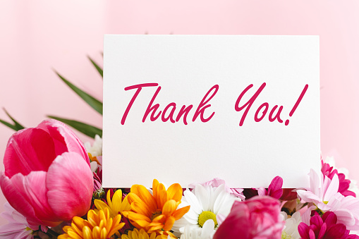 Thank you card in beautiful flowers bouquet on pink background. White blank card with space for text, frame mockup for invitation. Spring festive flowers.
