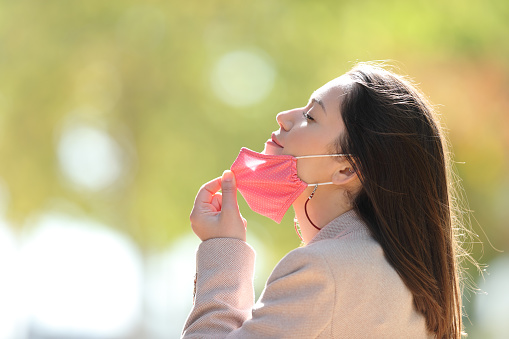Woman taking off mask breathing fresh air in a park