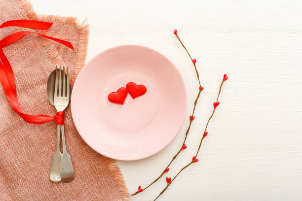 istock Valentines Day festive table setting on a white wooden table. Dinner meal in restaurant at Valentine Day. Two red hearts on pink plate. Valentine Day, love, romance, dating concept,copy space,flat lay 1282343092