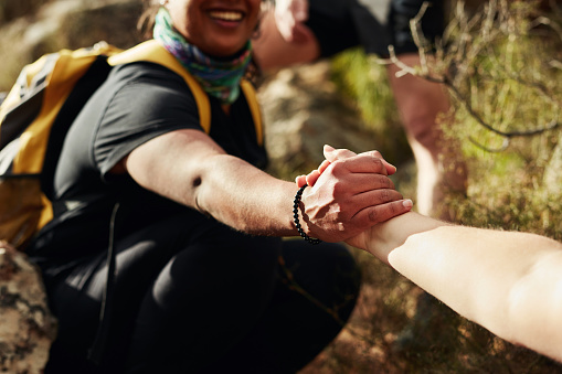 Cropped shot of two young women reaching for each other's hands on a hiking trail