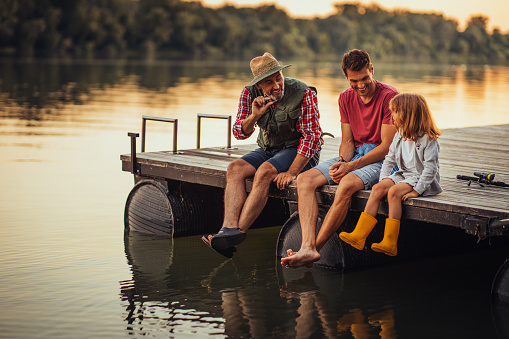Grandfather, father and grandson sitting on the pontoon and taking a break while fishing