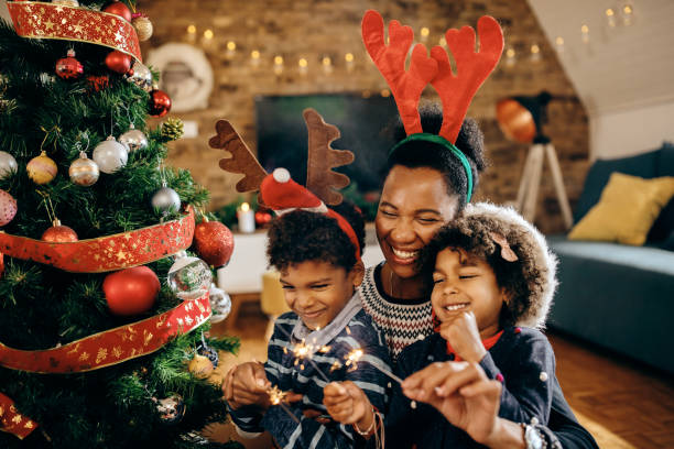 Joyful black family celebrating Christmas and having fun with sparklers at home. Happy African American children having fun with their mother while using sparklers on Christmas at home. family christmas stock pictures, royalty-free photos & images