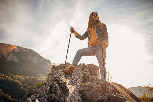 One beautiful young woman with backpack standing on the top of a mountain. Exploring the nature and enjoying in the landscape view.