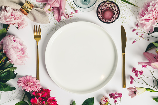 Elegant table setting with floral decor, flat lay. Wedding or festive table setting. Plate and cutlery with pink flowers on white background
