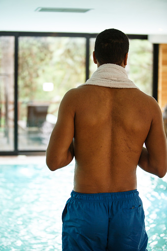 Rear view of young mixed race man standing at the poolside and looking at the swimming pool about to enter the water and have a relaxing swim.