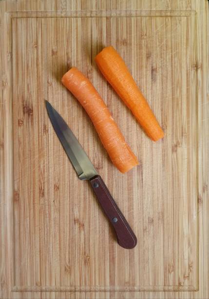 Top view of a wooden cutting board, with two carrots and a knife on it.  Background image for themes of cooking, recipes, food preparation. Background image for recipes, cooking at home, food preparation, template for nutrition concepts, healthy eating, with space for writing. agricultural themes stock pictures, royalty-free photos & images