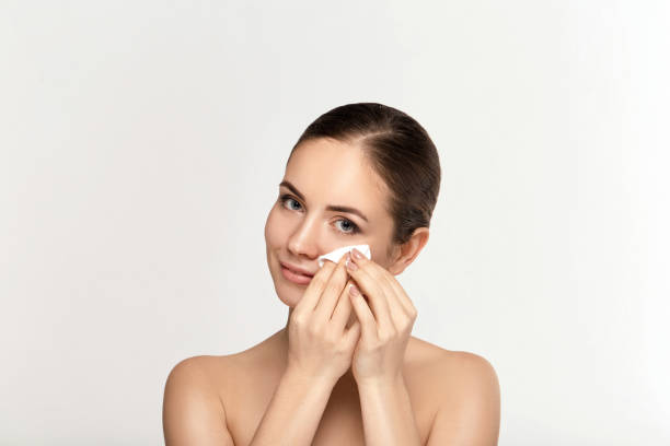 istock Cheerful woman removing face makeup with a cotton pad on white background 1282353191