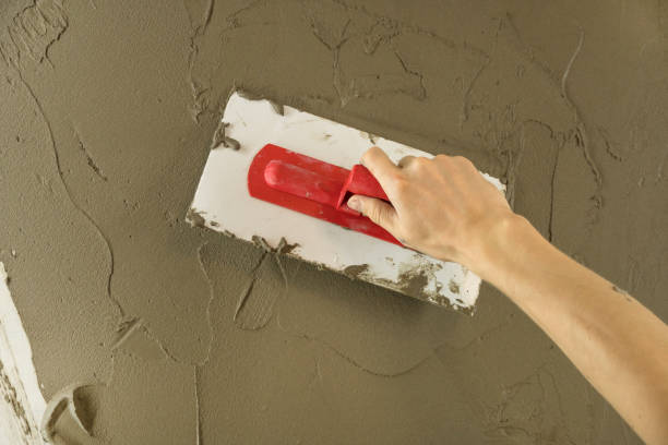 istock A worker plasters the wall with a spatula and applies a cement mix solution. The repairman lays the plaster on the drywall. Handyman repairs home. Laborer restore dwelling. Specialist covers up cracks 1282354811