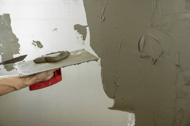 istock A worker plasters the wall with a spatula and applies a cement mix solution. The repairman lays the plaster on the drywall. Handyman repairs home. Laborer restore dwelling.Specialist covers up cracks 1282354812