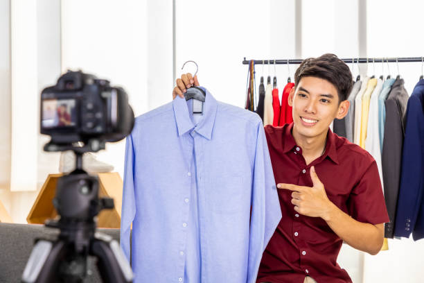 Young Asian male online merchant blogger using camera to live video to review and sell product. Social media, Influencer, and online shopping concept. Young Asian male online merchant blogger using camera to live video to review and sell product. Social media, Influencer, and online shopping concept. home recording studio setup stock pictures, royalty-free photos & images