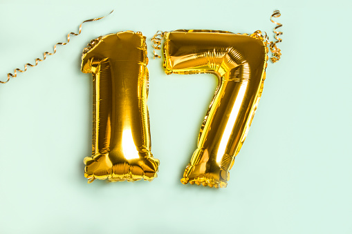 Decoration for seventeen birthday party. Golden balloon in form of 17 number on blue background