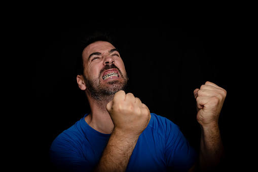 Bearded man wearing blue t-shirt with angry expression posing on black background. Disposal concept
