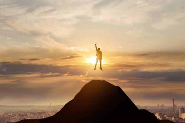 Leadership and business success concept. Businessman jumping on top of the mountain against the background of the city.