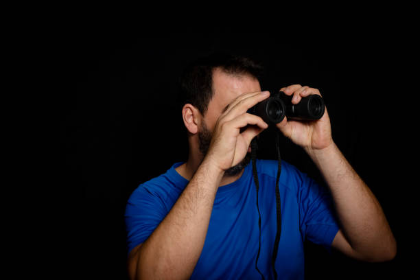 istock Bearded man dressed in blue t-shirt with binoculars posing against black background 1282362264