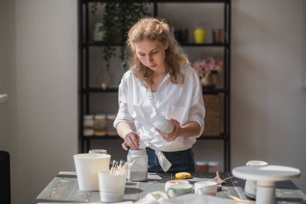 istock Female potter glazing raw unburned ceramic cup using brush. Earthenware mug putting colorant on pottery workshop 1282364032