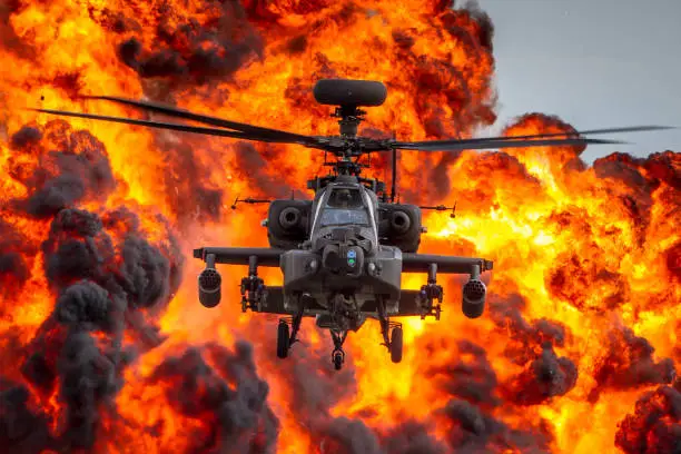 British Army AH64 Apache attack helicopter flying from an explosion of flames and smoke