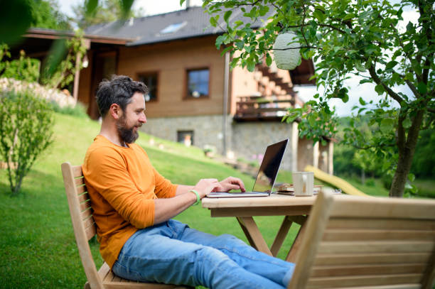 istock Side view of man with laptop working outdoors in garden, home office concept. 1282365556