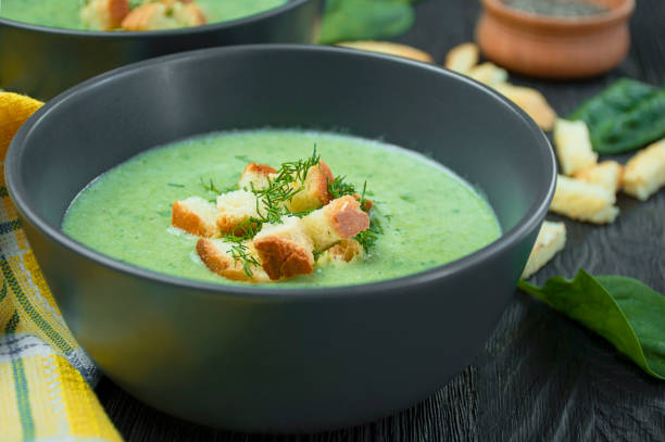 istock Spinach cream soup with crackers, herbs on a dark table. Green soup is served in a bowl on a wooden table. Side view. 1282368181