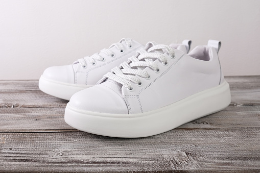 White leather casual sneakers on wooden background.