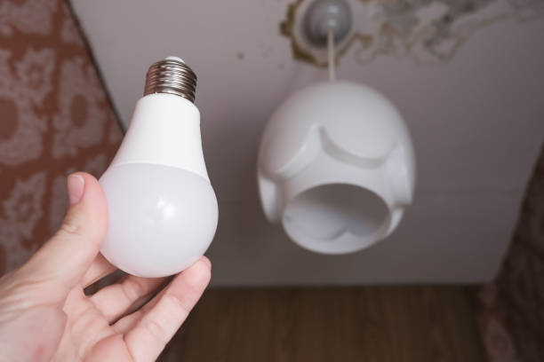 istock Female hand holding a led light bulb to change, replace it at home, screwing in the bulb into a lamp holder for energy saving and economy, saving money 1282370530