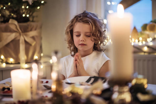 small girl sitting at the table indoors at christmas, praying. - color image jesus christ child people imagens e fotografias de stock