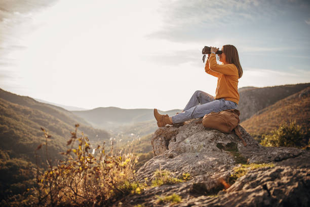 donna con binocolo seduta sulla vetta della montagna al tramonto - binocolo foto e immagini stock