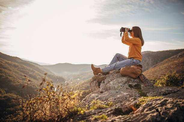 Woman with binoculars sitting on mountain peak in sunset One woman, female hiker sitting on mountain peak in sunset alone, looking at the view with binoculars. binoculars stock pictures, royalty-free photos & images