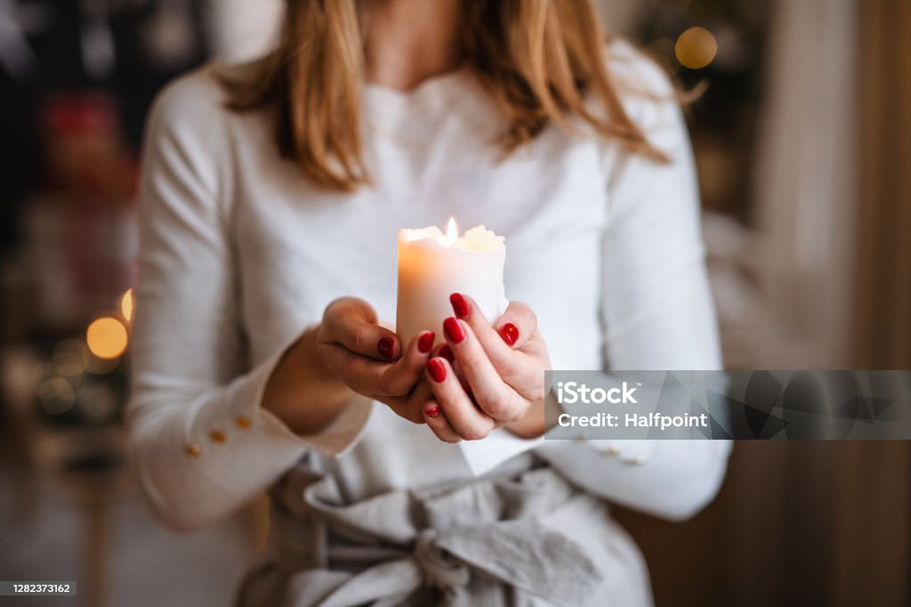 Unrecognizable young woman indoors at home at Christmas, holding candle. Unrecognizable young teenager woman indoors at home at Christmas, holding candle. Candle Stock Photo