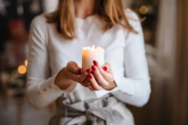 Photo of Unrecognizable young woman indoors at home at Christmas, holding candle.