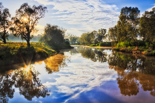 Reflection of the sun in calm still waters of Macquarie river at sunrise in Dubbo city of Australia.