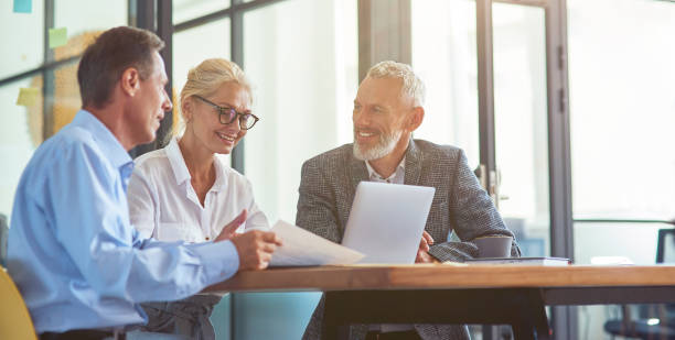 istock Successful business people working together, three happy coworkers interacting, discussing something and smiling while sitting at desk in the modern office or coworking space 1282375710