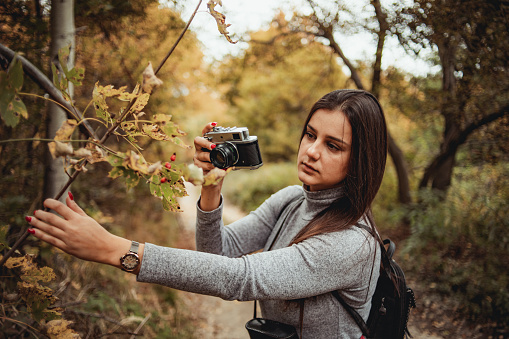 Young woman photographing the autumn season - Woman in the woods during warm color fall