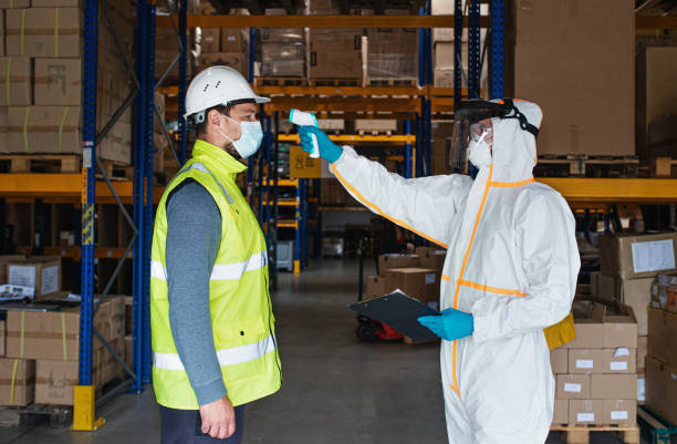 istock Workers with face mask and suit in warehouse, coronavirus and temperature measuring concept. 1282377997