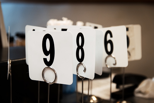 A bunch of restaurant table number in a cluster on a countertop. The numbers are black on white backgrounds, held by silver looped stands.