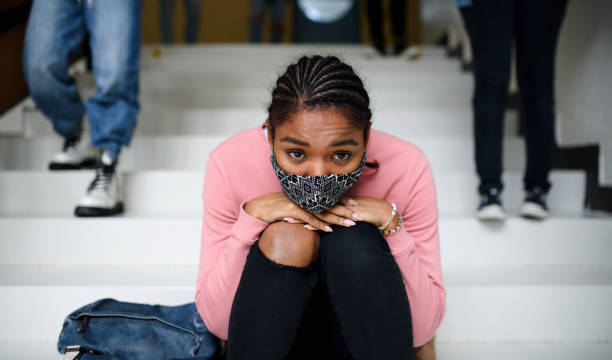 istock Depressed young student with face mask sitting on floor back at college or university, coronavirus concept. 1282383582