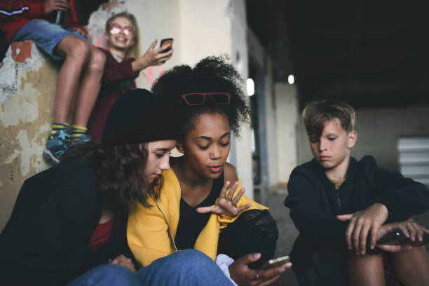 groupe d’adolescents gang assis à l’intérieur dans le bâtiment abandonné, en utilisant des smartphones. - youth culture gang member adolescence family photos et images de collection