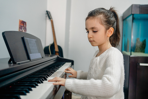 Beautiful little preschool girl playing piano at music school. Cute child having fun with learning to play music instrument. Early musical education for children.