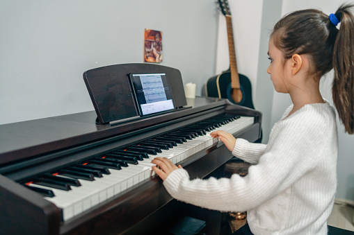 Side view of girl playing piano. Cute female child is practicing on musical instrument. She is at home.